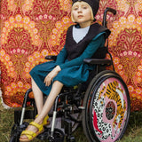 Girl wearing the black cat costume sitting in her wheelchair against a pink floral fabric backdrop.