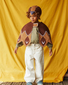 Child wearing the brown duck hat and brown feathered bird cape, standing in front of a yellow fabric background.