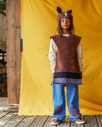 Child wearing the brown horse hat and tabard, standing in front of a bright yellow fabric background.