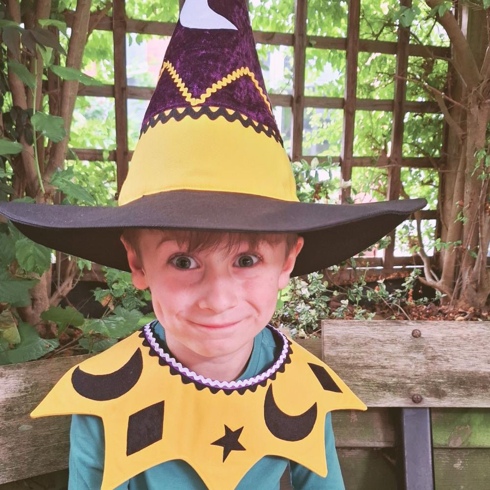 Smiling child wearing the celestial moon and stars kids costume collar and witch hat sitting outdoors.
