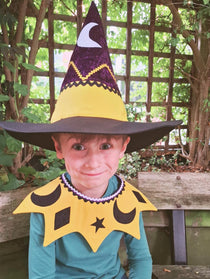 Smiling child wearing the celestial moon and stars kids costume collar and witch hat sitting outdoors.