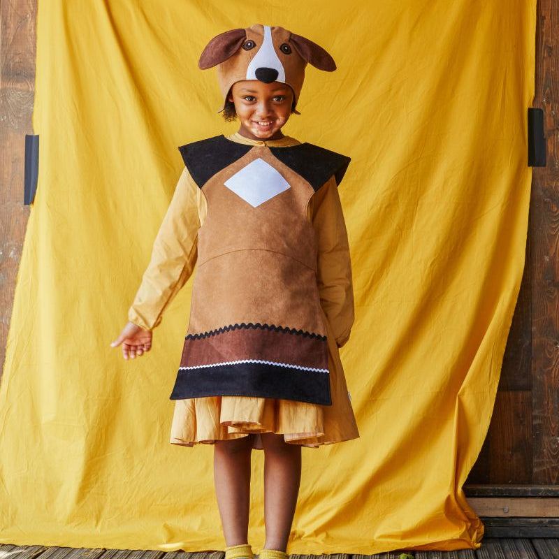 Child wearing the floppy eared dog hat and tabard, smiling at the camera. She is standing in front of a yellow fabric background.