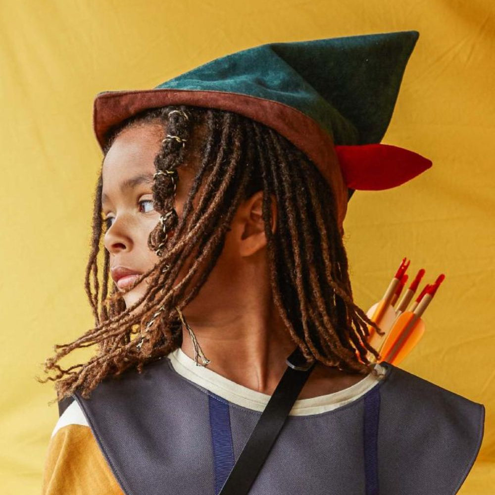 Boy wearing the green Robin Hood hat looking sideways against a yellow fabric background.
