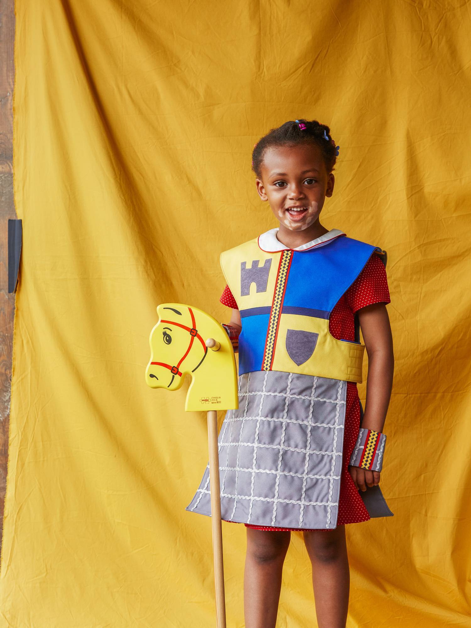 Girl carrying a yellow hobby horse and wearing the fairytale knight tabard and cuffs
