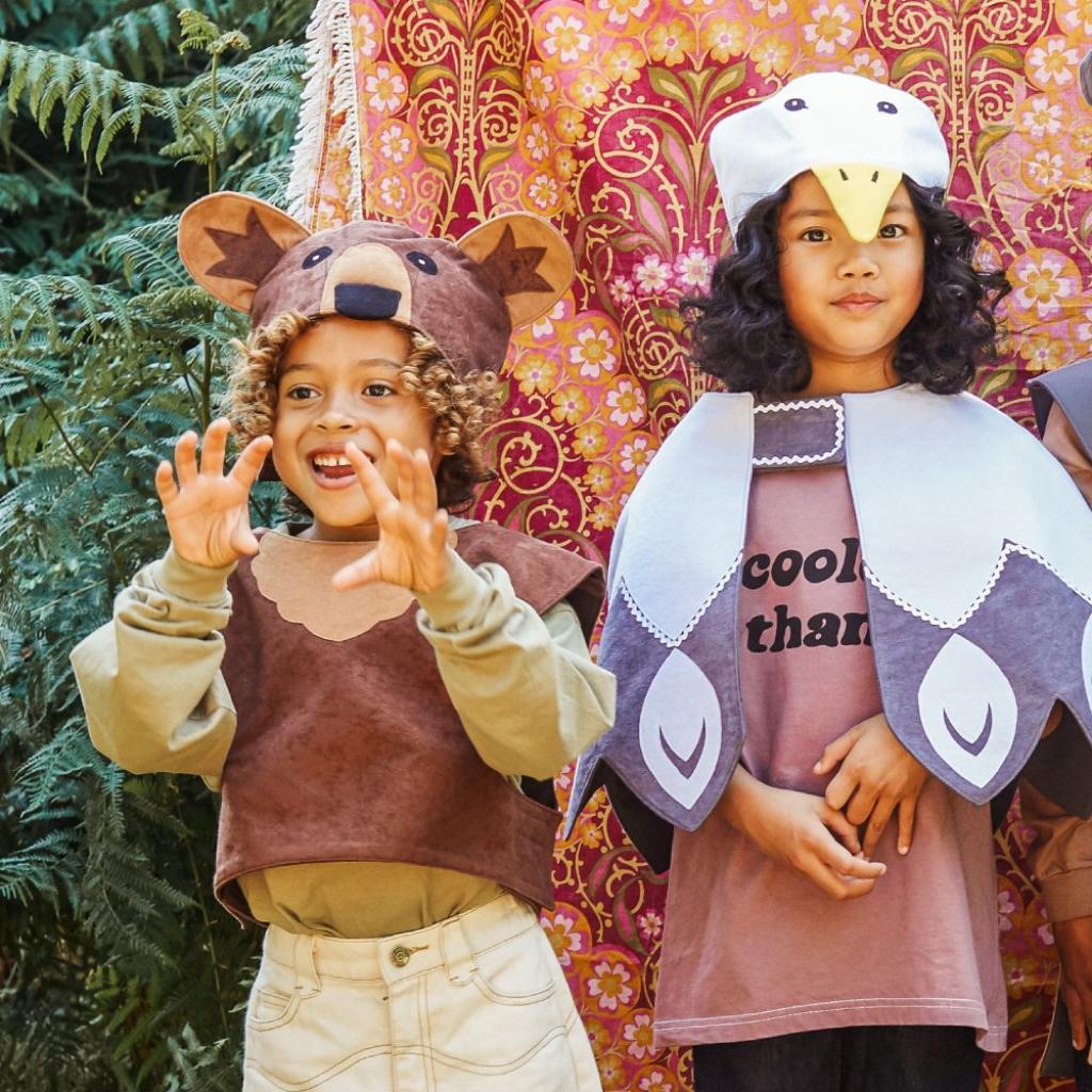 Two children in animal costumes standing in front of a colorful, patterned backdrop.