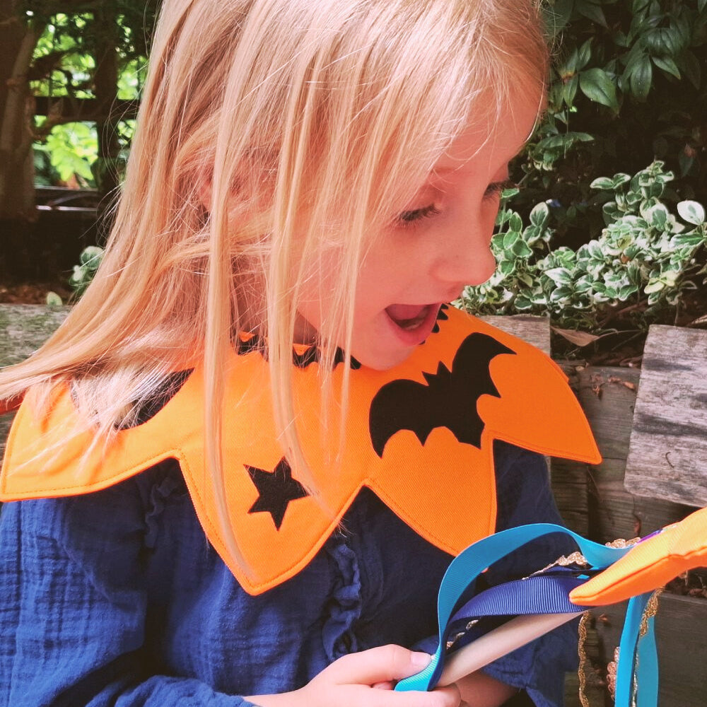 Smiling child wearing the magical pumpkin kids costume collar and holding the fairytale star wand sitting outdoors.
