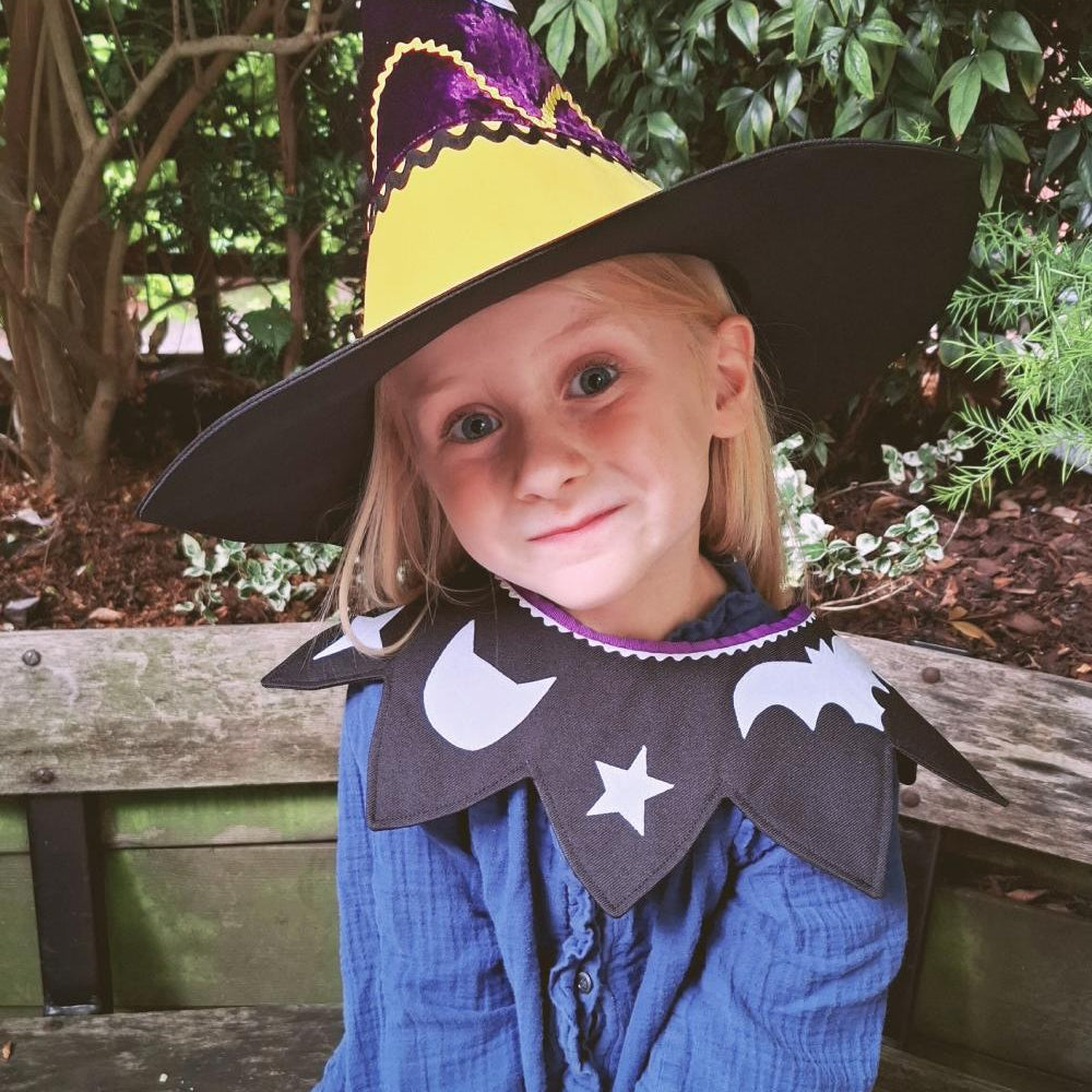 Smiling child wearing the magical pumpkin kids costume collar and witch hat sitting outdoors.