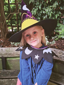 Smiling child wearing the magical pumpkin kids costume collar and witch hat sitting outdoors.