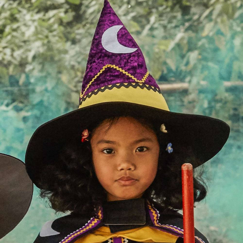 Girl wearing the magical witch hat and witch dress, holding a broomstick.