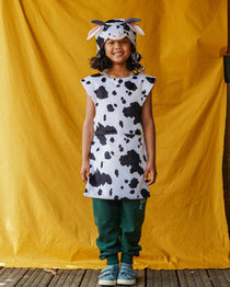 Child wearing a cow print dress and hat against a yellow backdrop