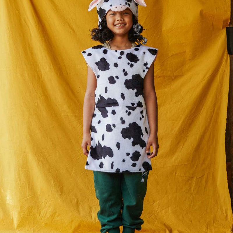 Child wearing a cow print dress and hat against a yellow backdrop