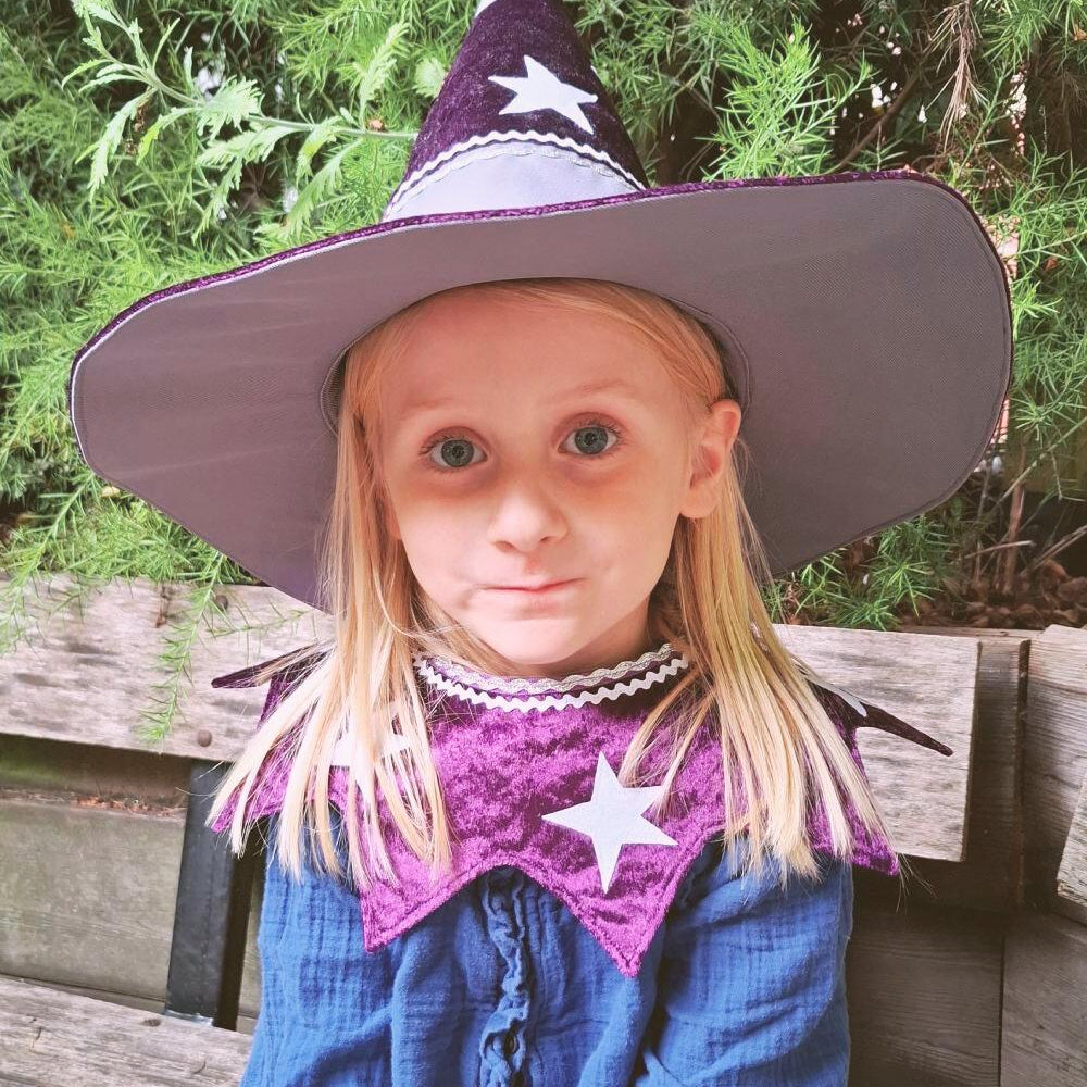 Girl wearing the starry wizard hat and twinkling stars kids costume collar, sitting outside in a garden.