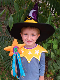 Smiling child wearing the twinkling stars kids costume collar, magical witch hat and holding the orange fairytale star wand, sitting outdoors.