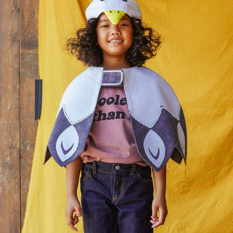 Child wearing the white feathered bird cape standing in front of a yellow fabric background.