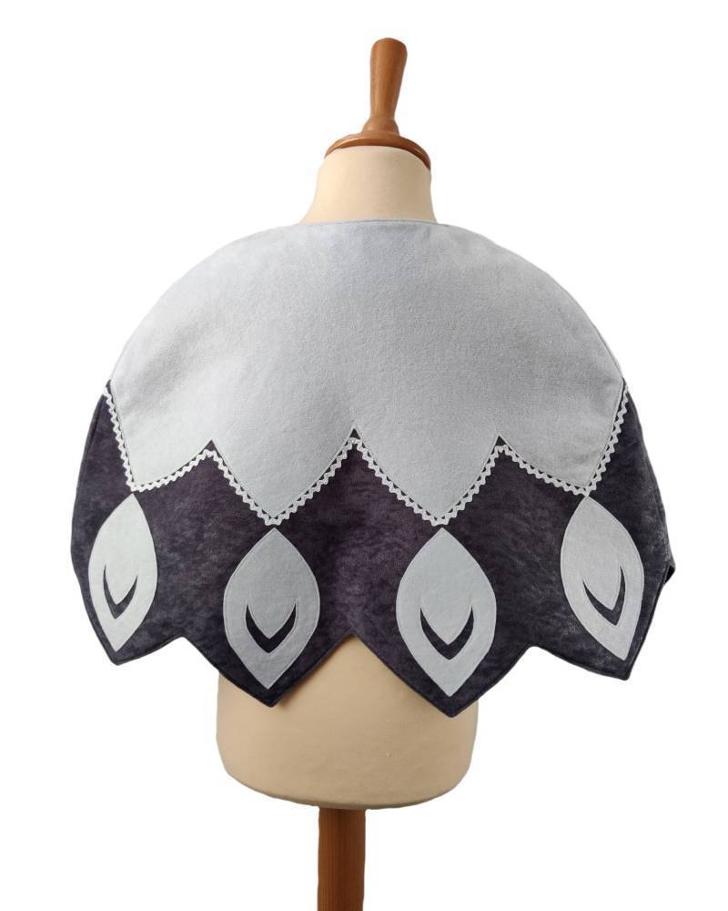 Back view of white feathered bird cape on a stand against white background.