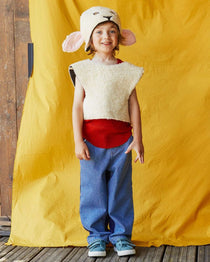 Child smiling at the camera wearing the woolly sheep costume, standing in front of a yellow fabric backdrop.