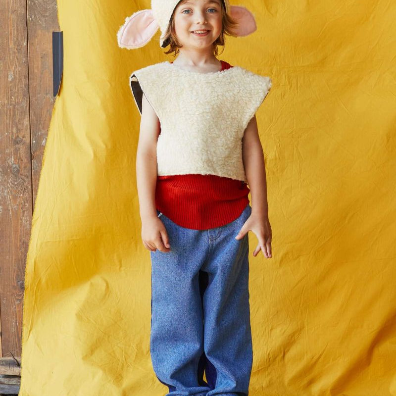 Child smiling at the camera wearing the woolly sheep costume, standing in front of a yellow fabric backdrop.