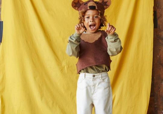 Child wearing a bear costume with a yellow curtain background